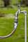 A silver outdoor tap with an orange-grey coupling attached to a garden hose, against a green background.