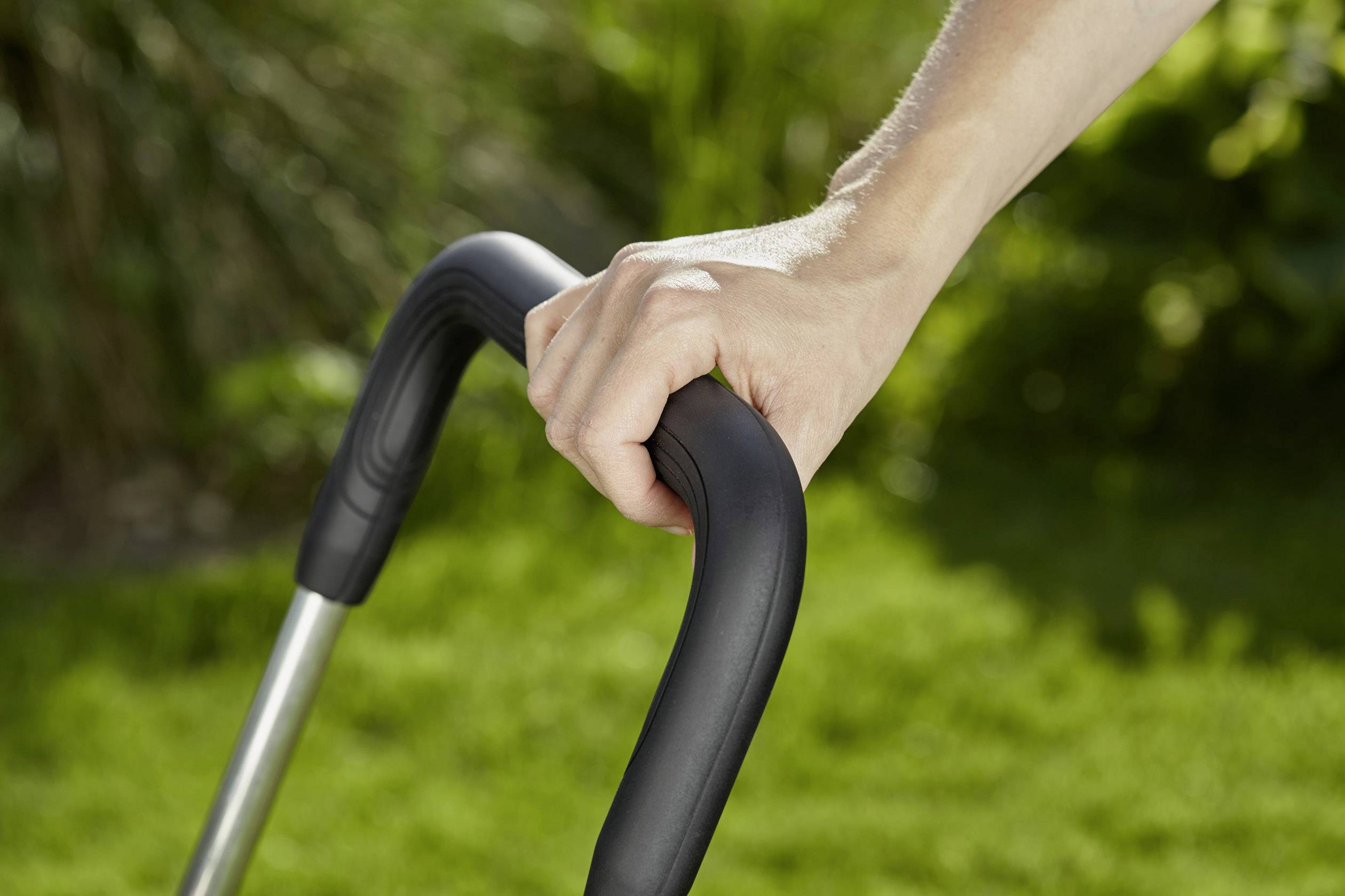 A hand is gripping the handle of a lawnmower on a green lawn.