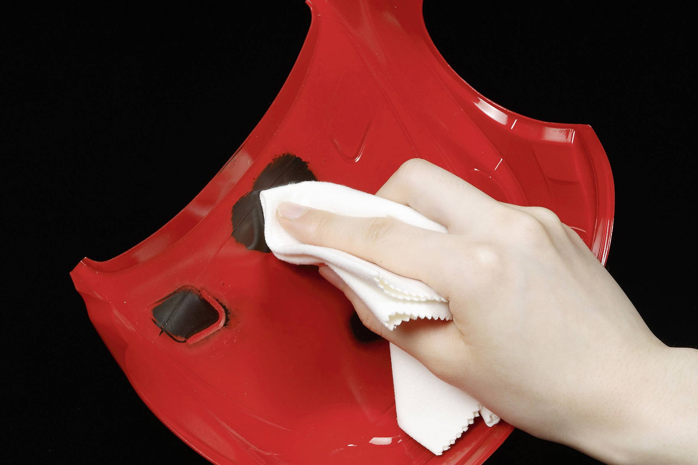 A hand is cleaning a red motorcycle helmet with a white cloth.