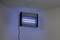 An electric insect killer hangs from the ceiling, illuminated with blue light, designed to attract insects in a room.