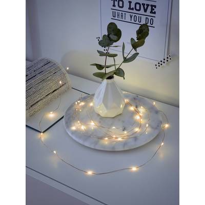 A small vase with eucalyptus branches sits on a marble plate, surrounded by fairy lights. In the background, a picture reads 'To Love What You Do'.