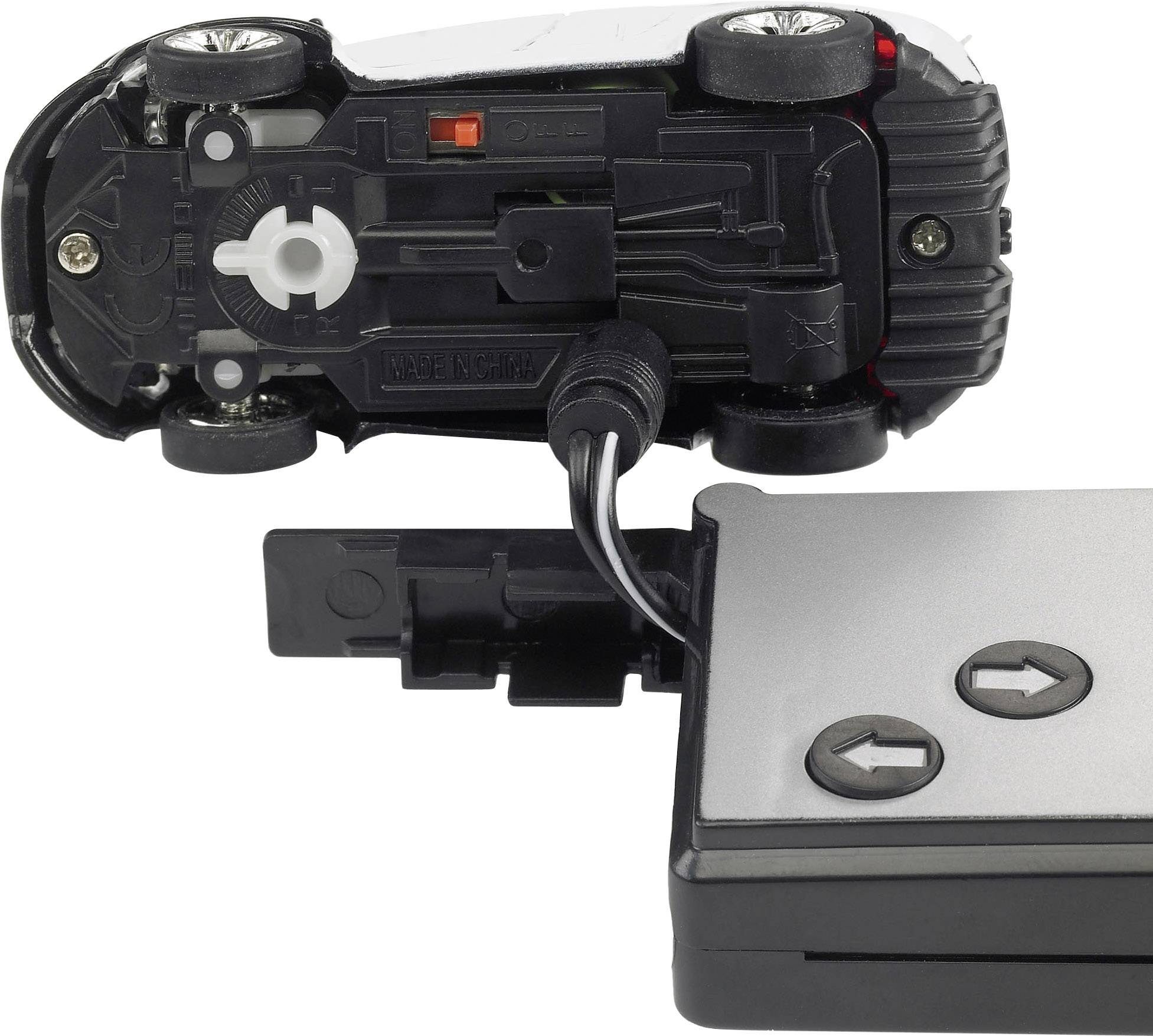A toy car lies on its side, connected to a remote control. It shows the underside and drive mechanism.