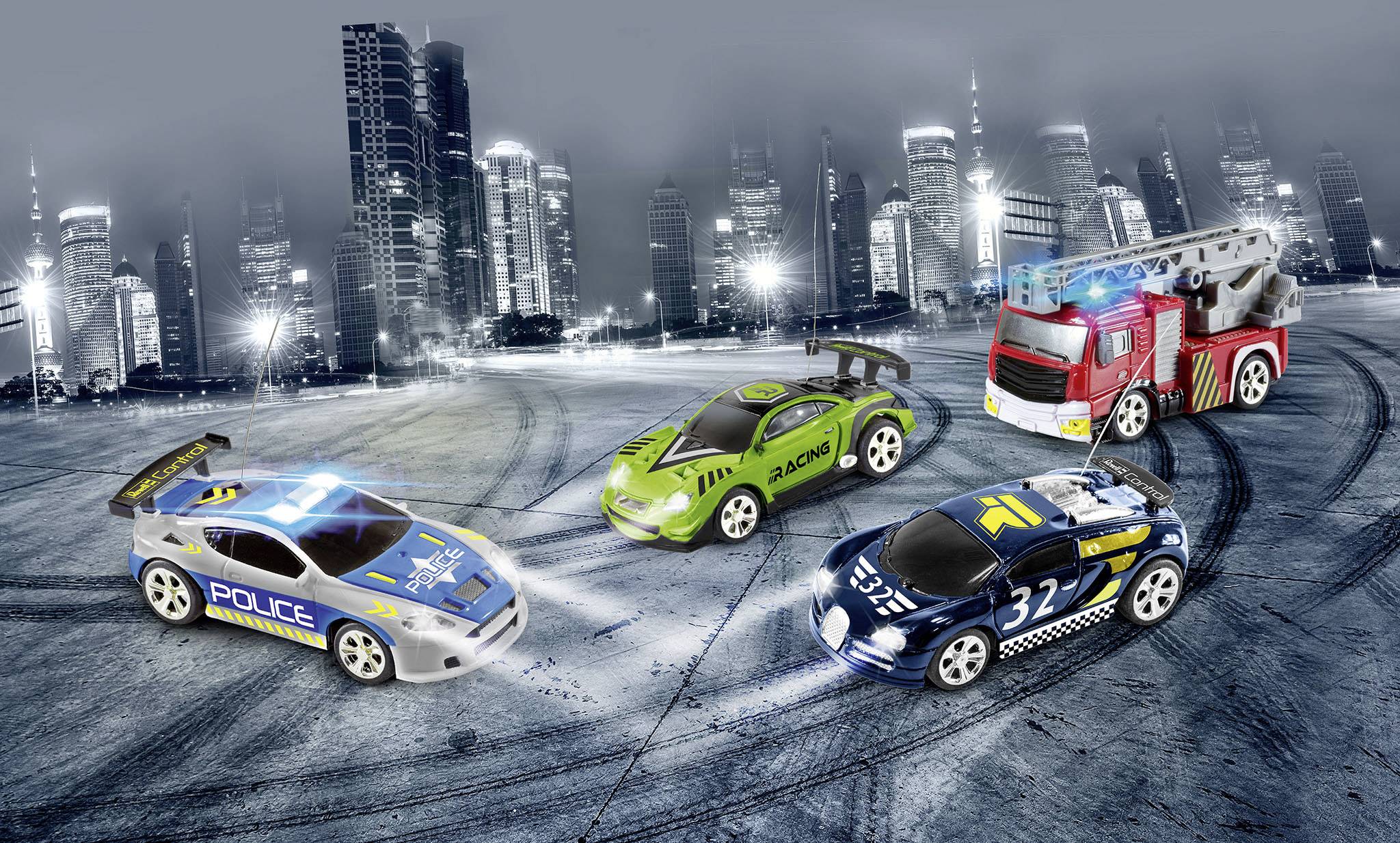 Four toy cars on an urban street at night: a police car, a green car, a racing car, and a fire engine.