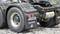 Close-up of a model lorry rear with the number plate 'SCMODEL'. The background shows a rocky surface.