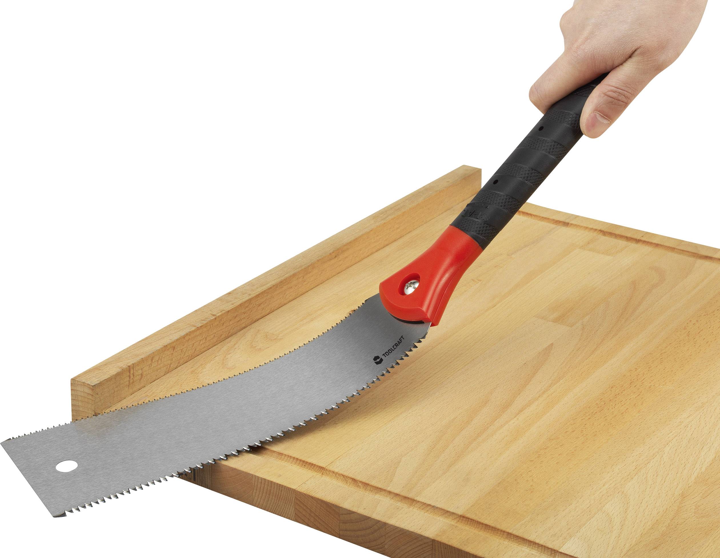 A hand is holding a handsaw with a red and black handle, which is resting on a wooden board.