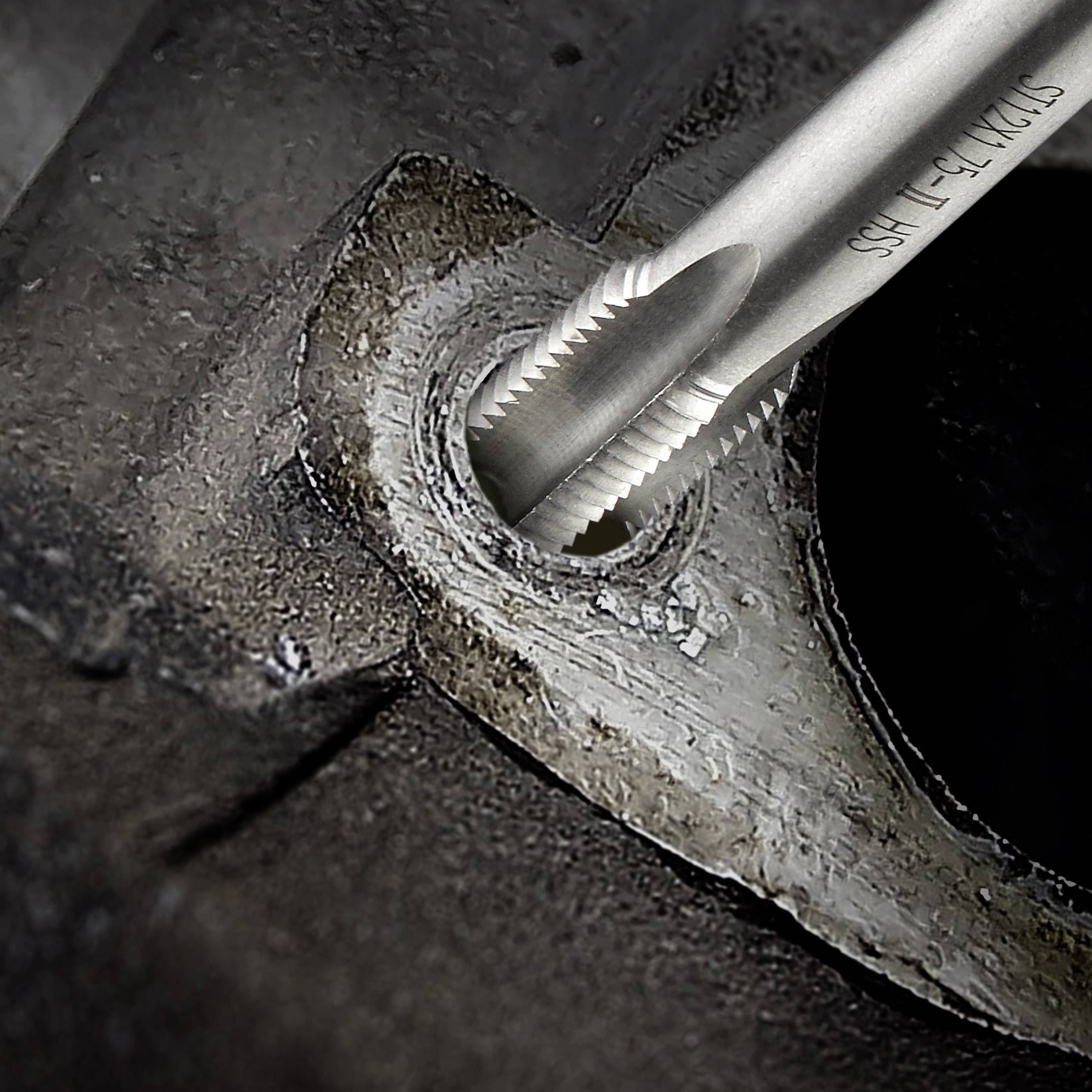 A tap cuts a thread into a metal piece. The surrounding area shows metal shavings and the rough surface of the workpiece.