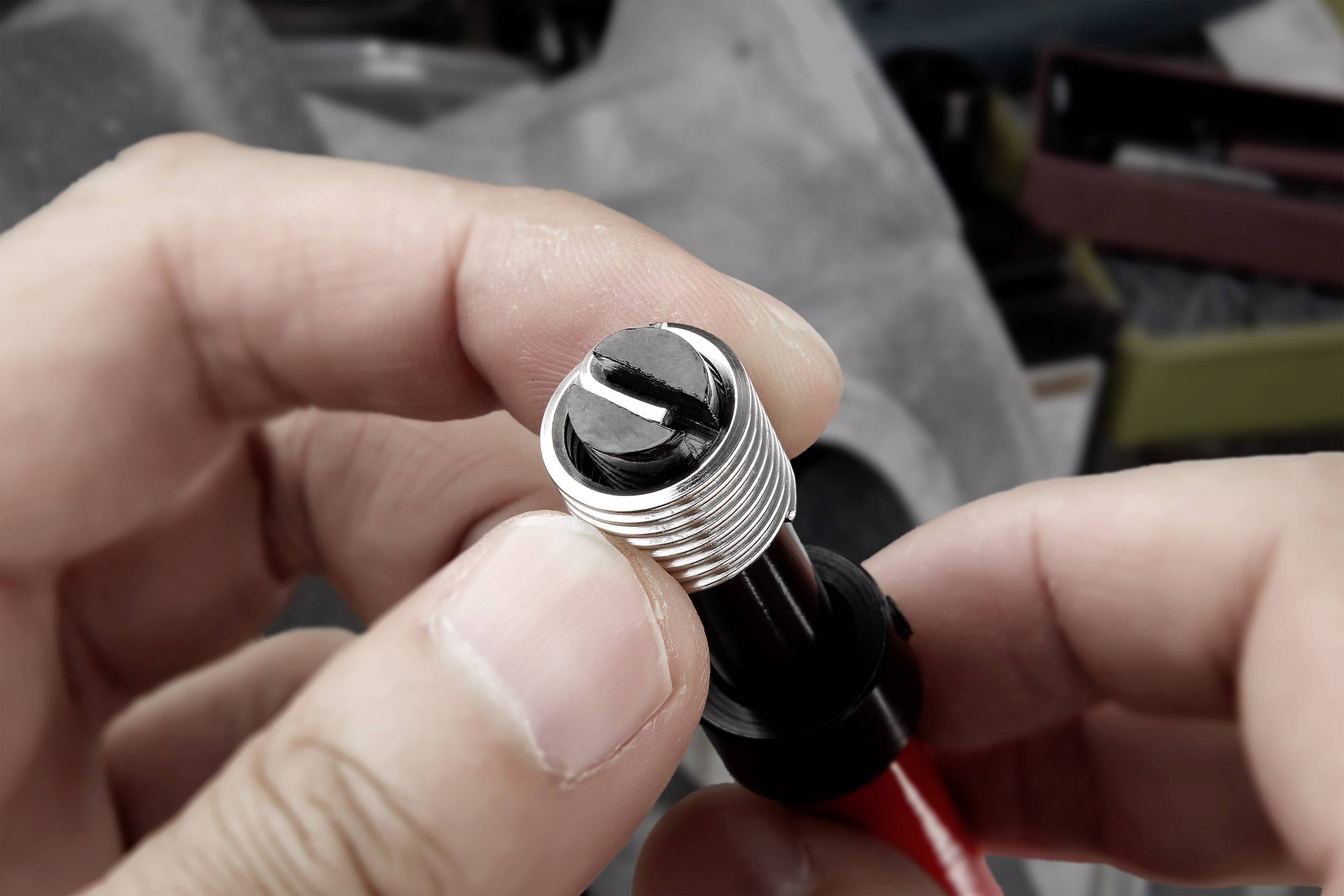 A person is holding a small, silver, cylindrical metal component with a black screw, possibly part of a technical device.