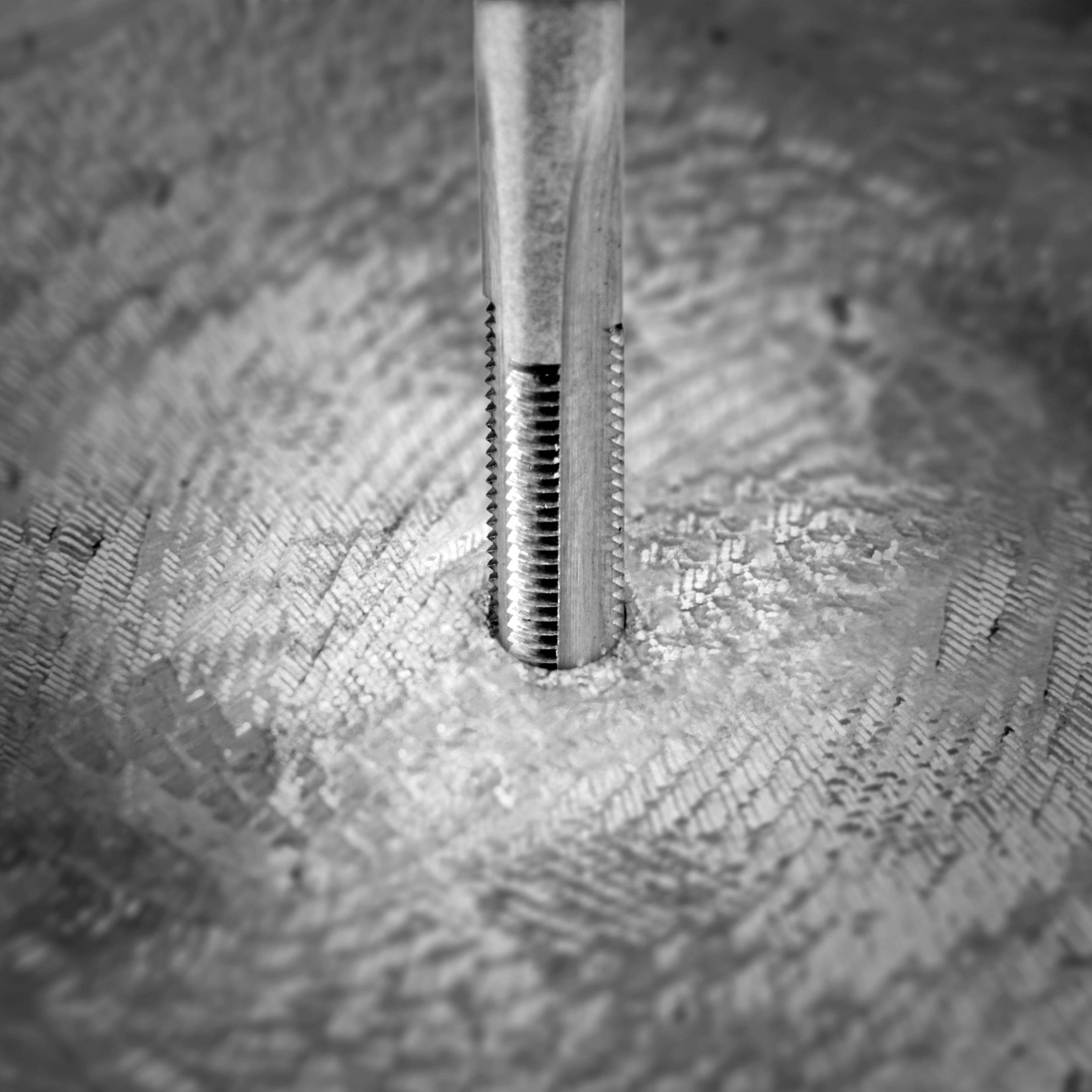 Close-up of a metal drilling operation with a tap cutting a precise thread into a metallic textured surface.