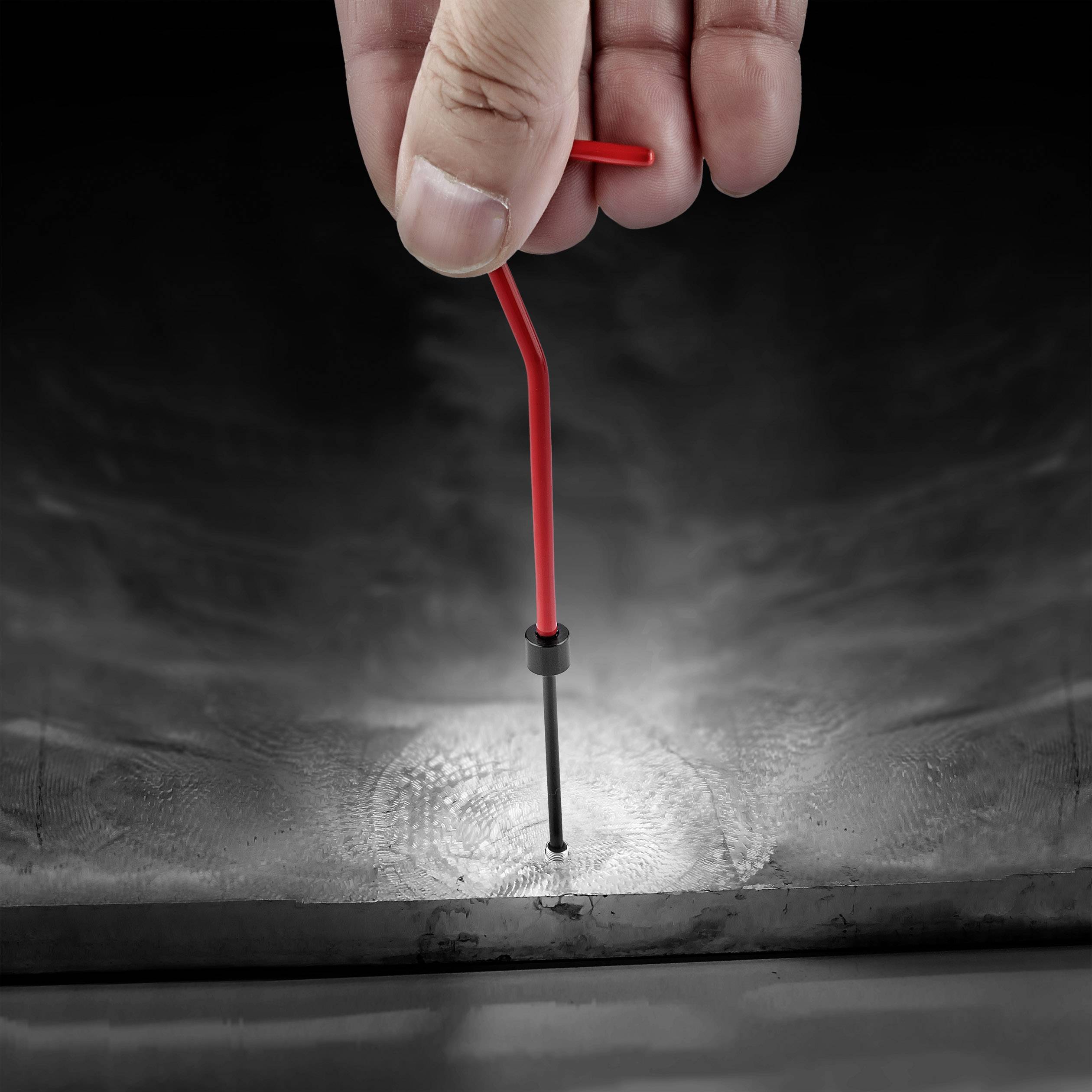 A hand pulls a red key from an angled surface. The key is positioned in a cylindrical shaft.