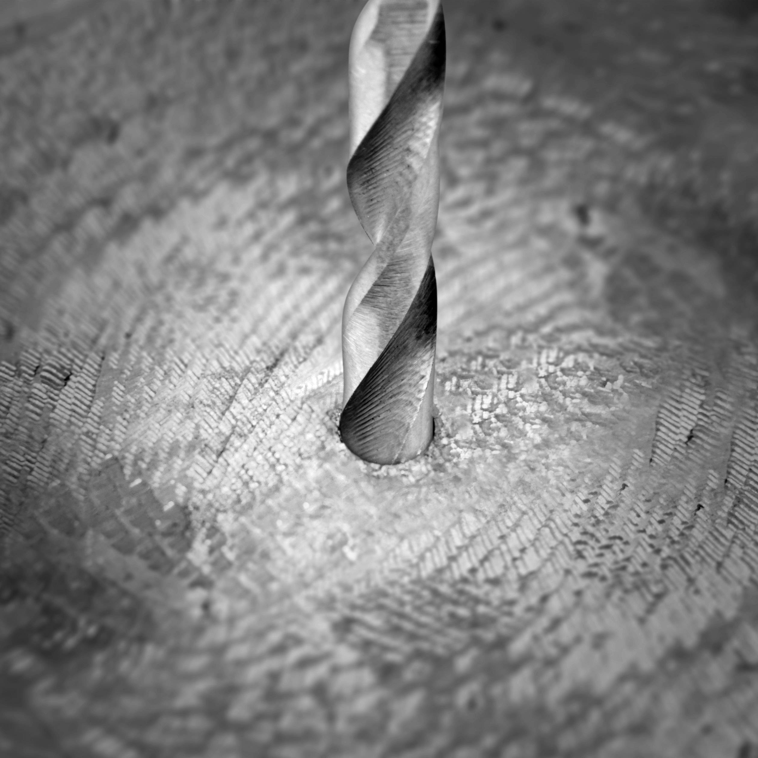 Close-up of a drill bit penetrating a metallic surface. The rotational movement generates spiral-shaped chips around the drill hole.