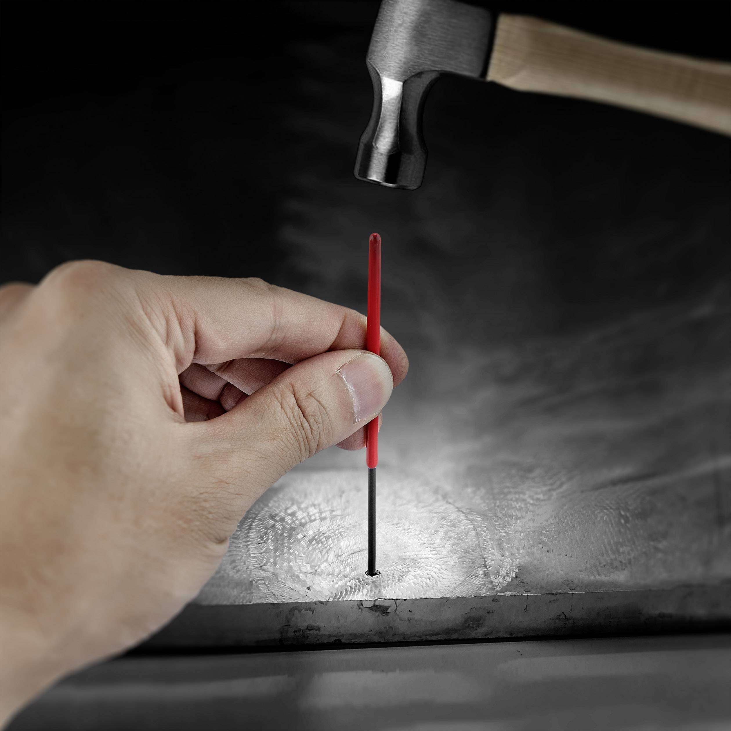 A hand is holding a red nail against a metal surface. A hammer is poised to strike the nail.
