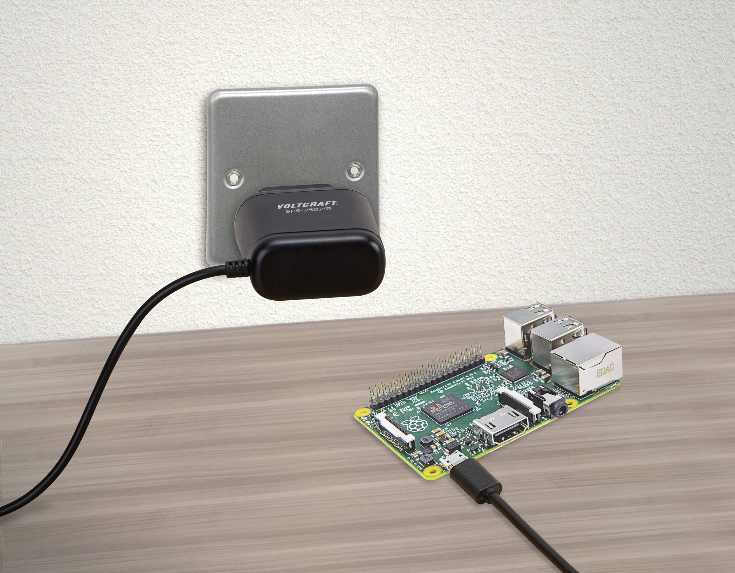 A charger is plugged into a socket and connected to a small computer, such as a Raspberry Pi, on a table.