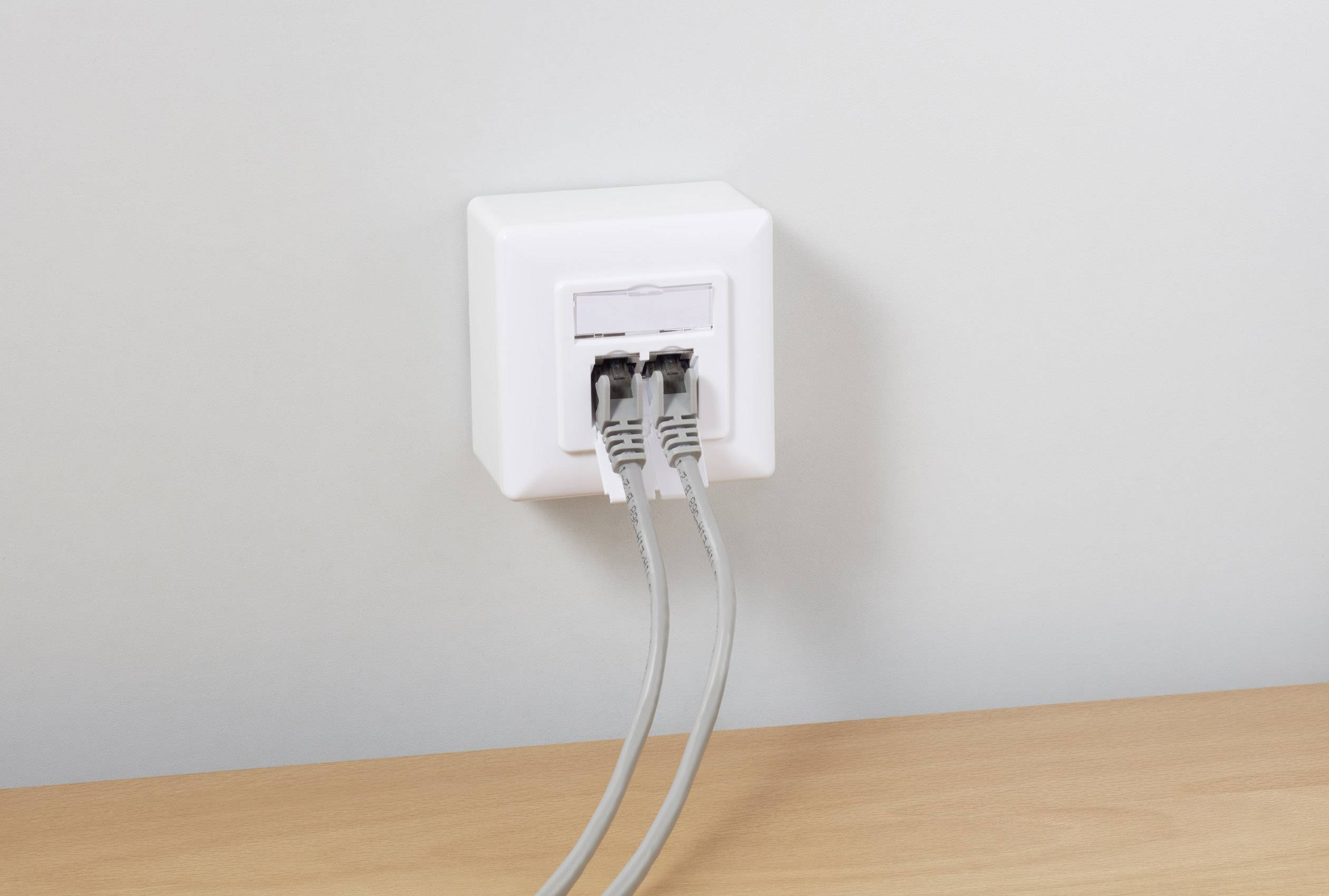 A wall socket with two plugged-in network cables leading to a wooden table.