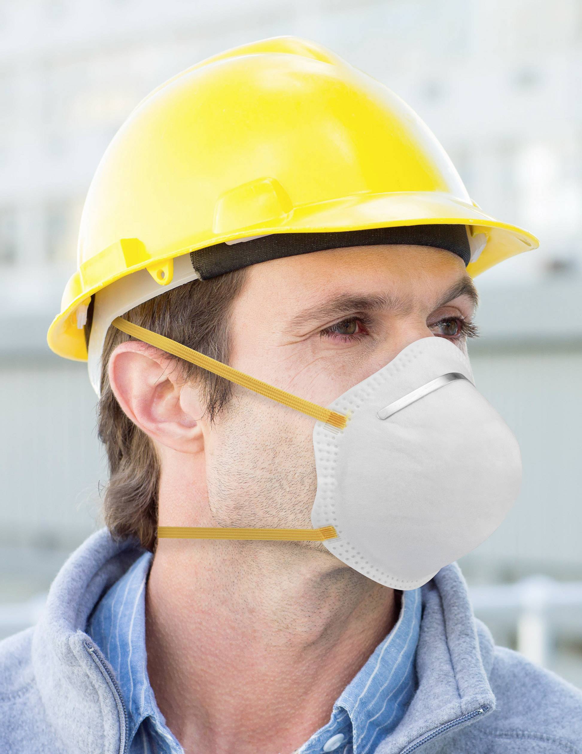 A construction worker wearing a yellow hard hat and respirator mask looks to the right. Background is blurred, with a construction site environment visible.
