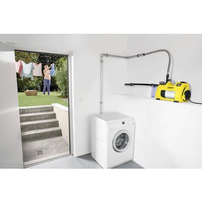 A utility room with a washing machine. A person is hanging laundry on a washing line outside. A yellow device is mounted on the wall.