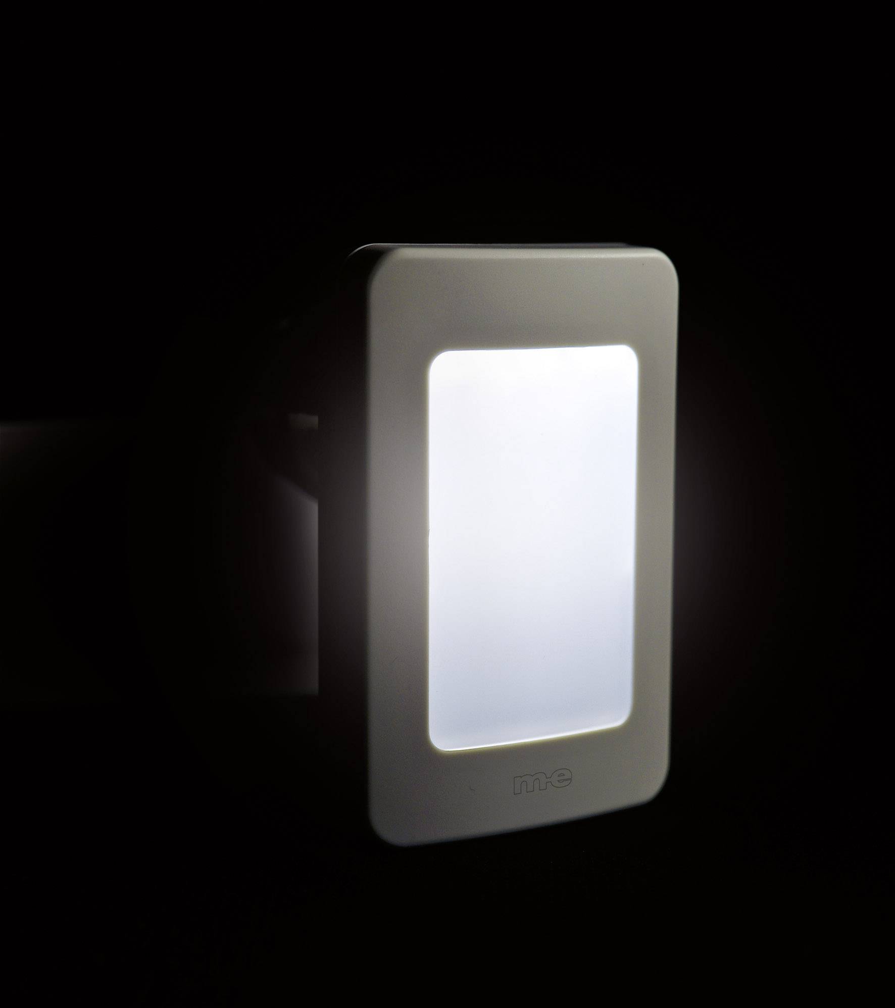 Nightlight plugged into a wall socket, glowing softly in the dark, rectangular in shape, with a white frame.