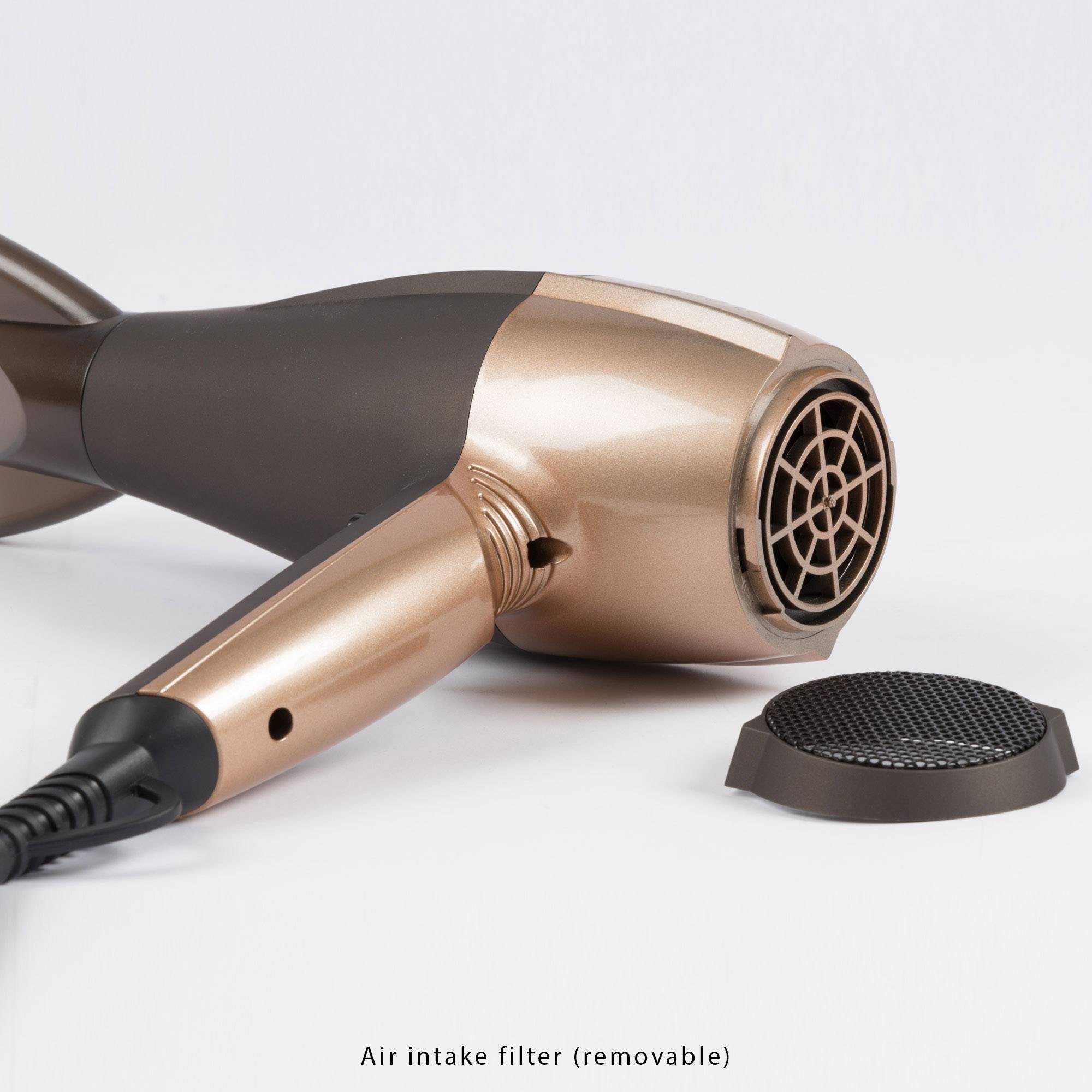 A hairdryer is resting on a surface with a distant air intake filter beside it. The hairdryer is a bronze colour.