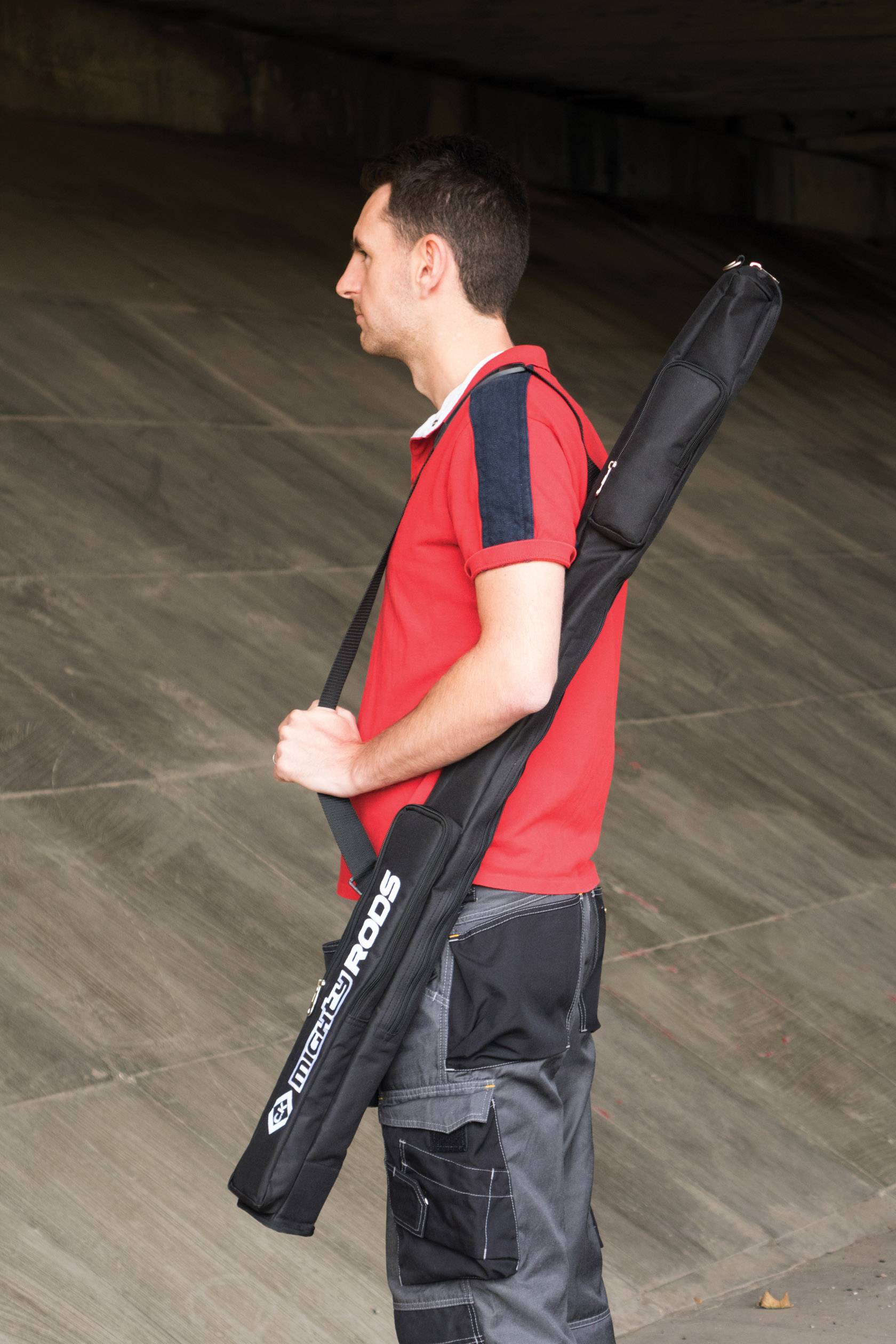 A man in a red T-shirt is carrying a large, black bag over his shoulder, standing in an urban setting.