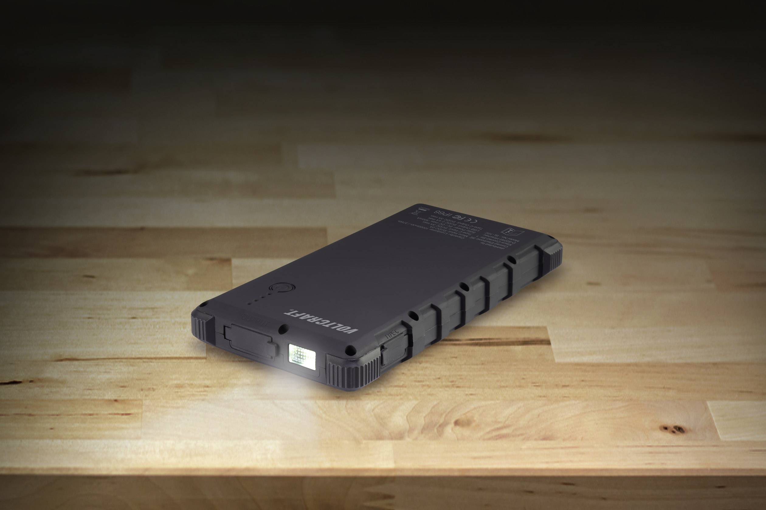 A black portable SSD drive lies on a wooden table. It has a compact, robust design and shows a small green light.
