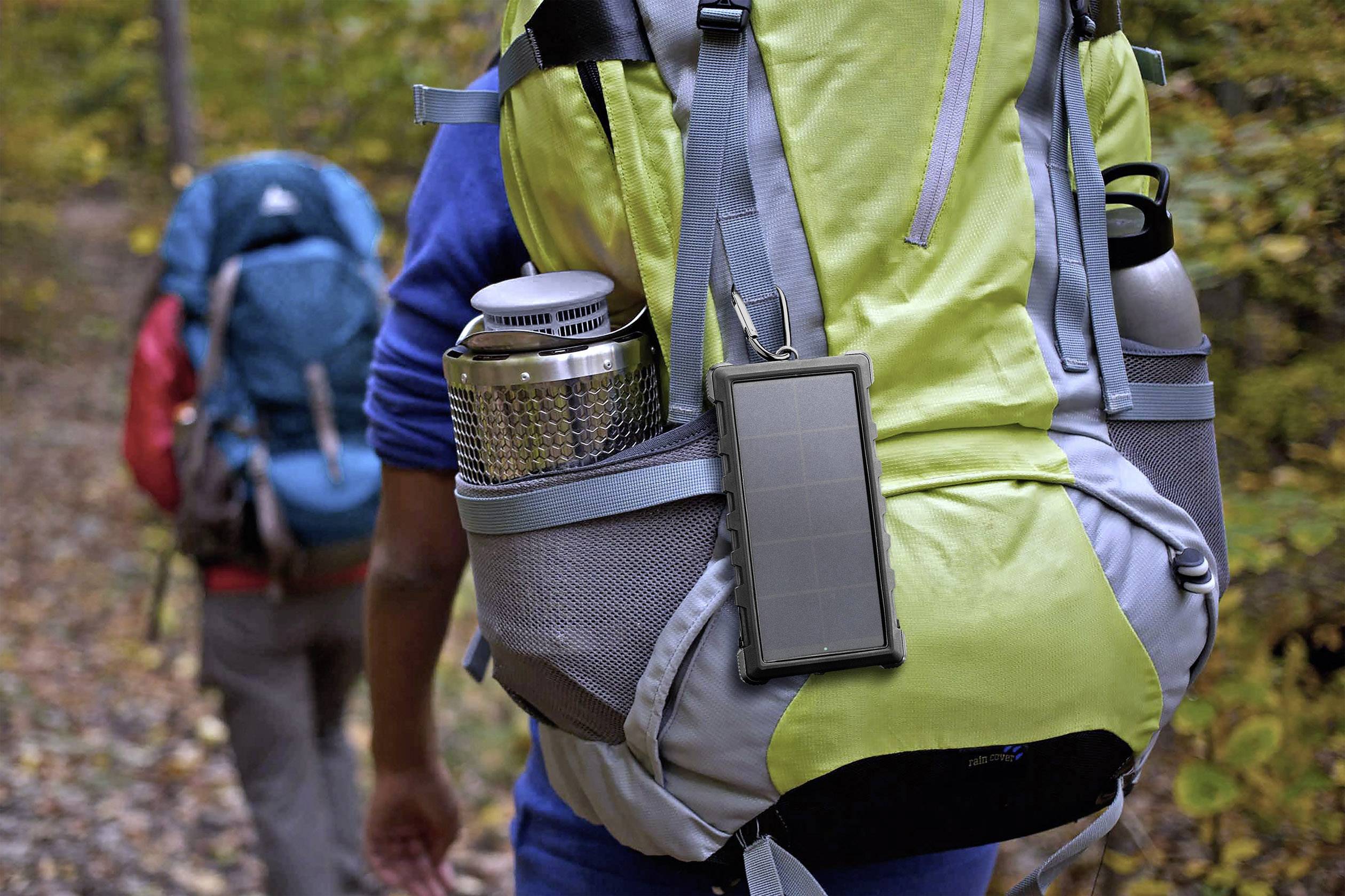Two people are walking along a woodland path. The person in front is wearing a green rucksack with an attached solar panel.
