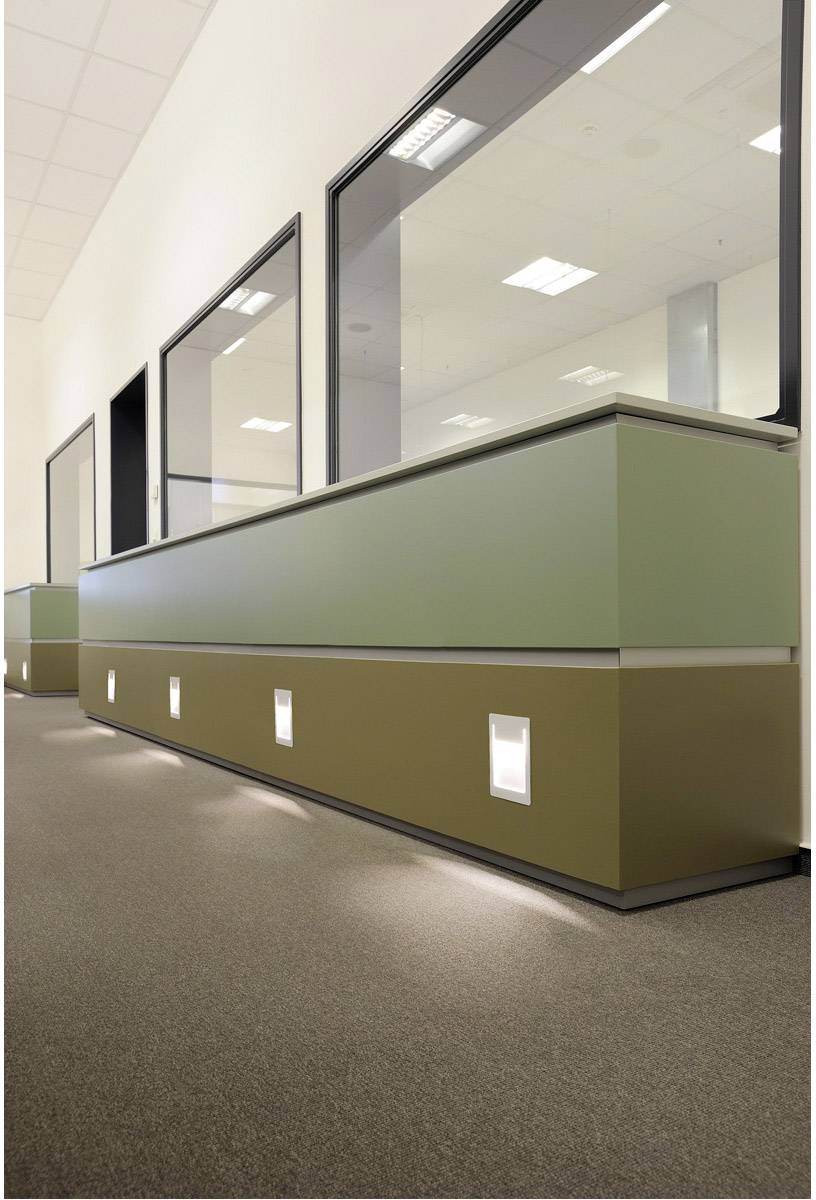 Reception area with a modern counter in green and brown tones, illuminated from below. Background with large windows and a bright ceiling.