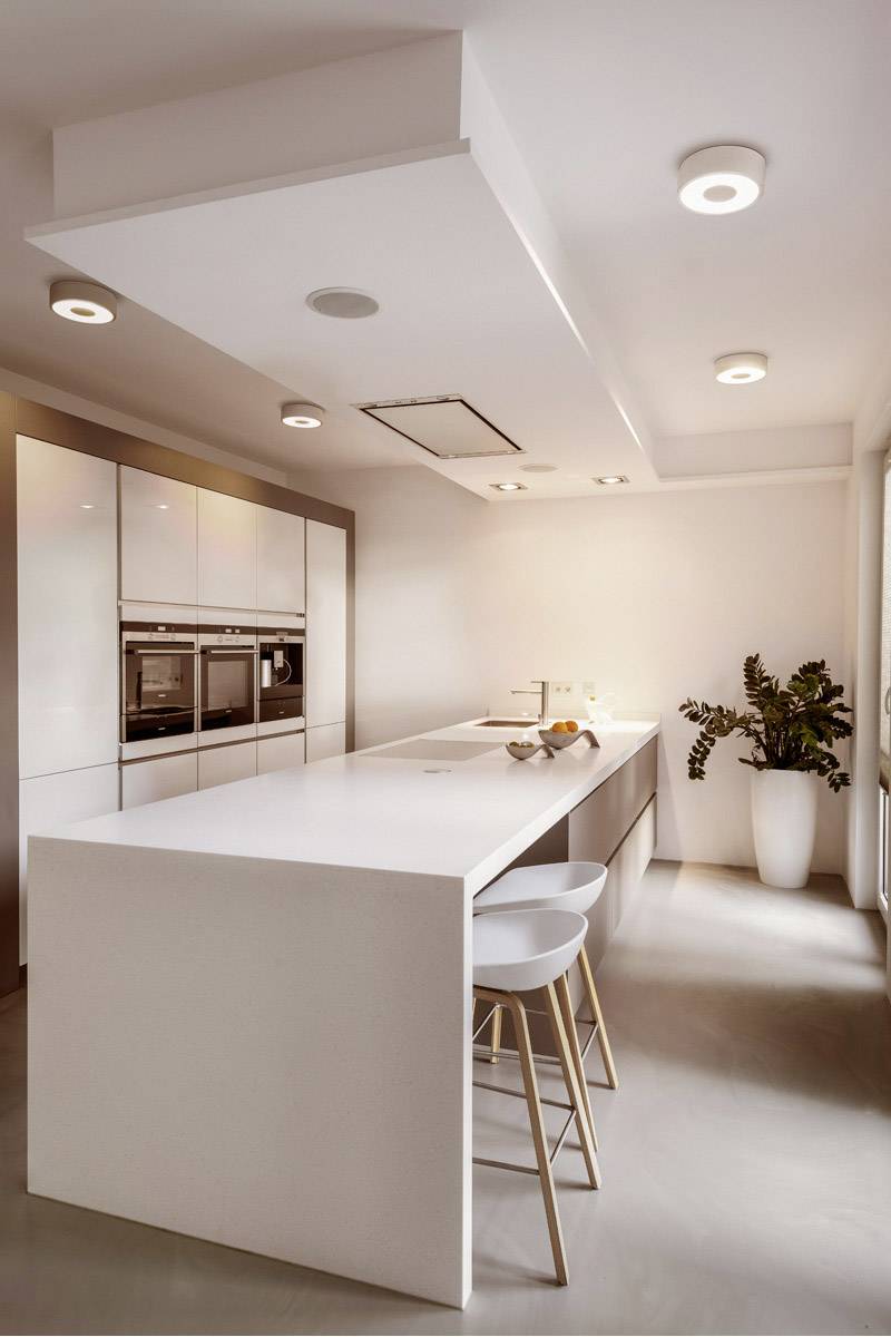 Modern kitchen with white cupboards, a large kitchen worktop and integrated hob. Two bar stools are positioned at the worktop.