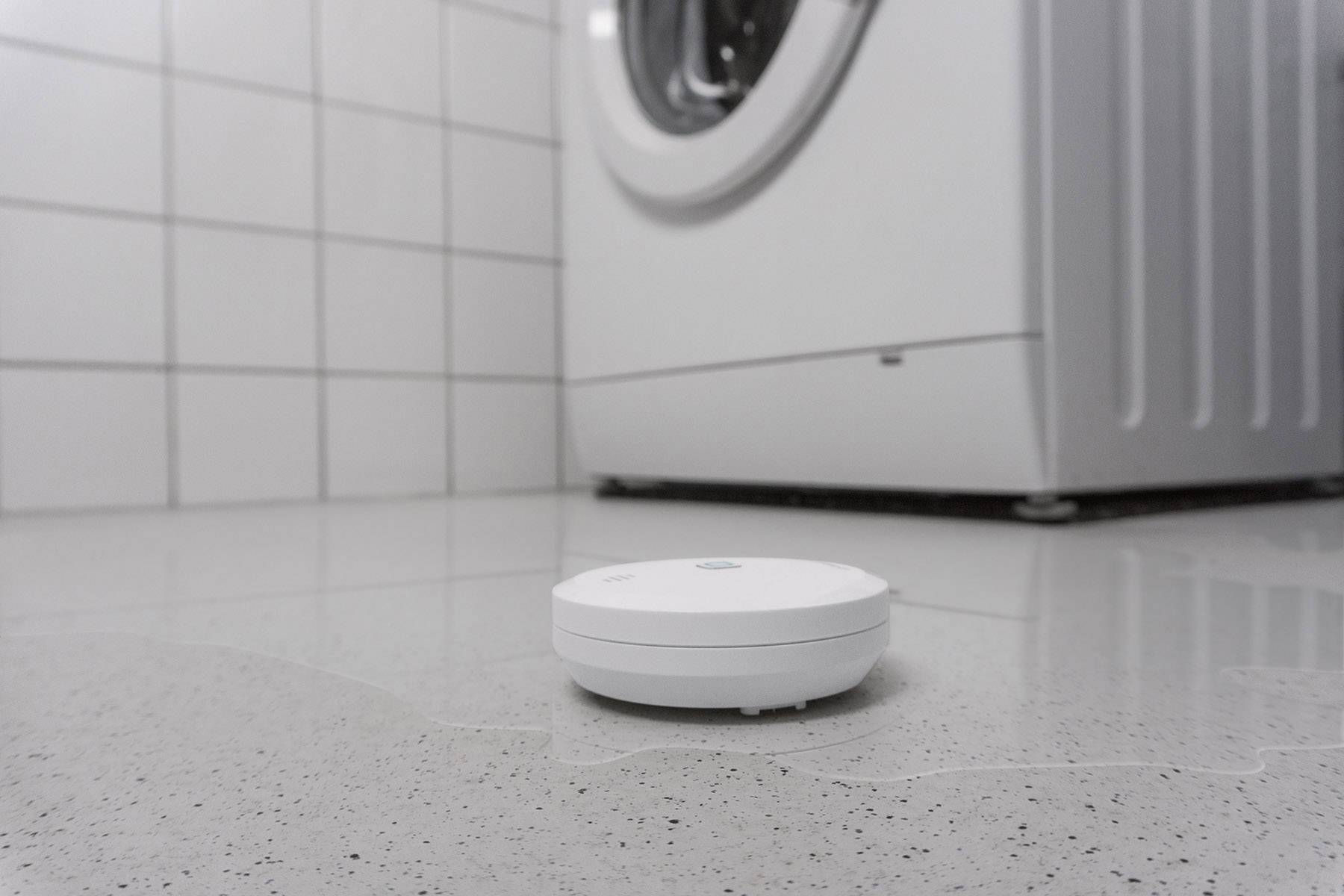 A sensor is lying on a wet floor in front of a washing machine.