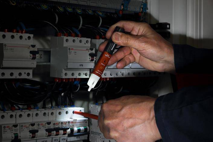 A person is testing the electrical voltage in a control cabinet using a voltage tester.