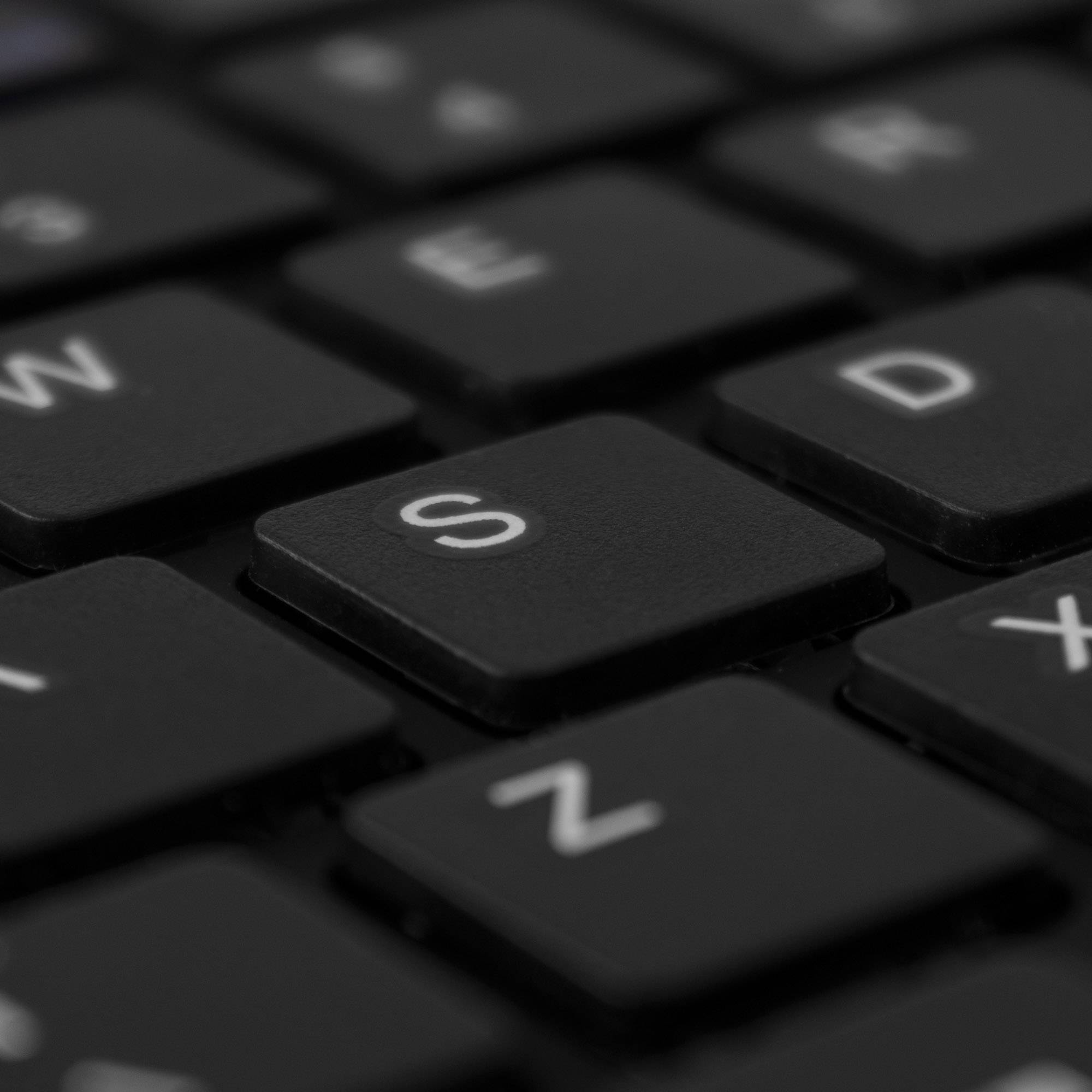 Close-up of a black computer keyboard with the 'S' key distinctly highlighted in focus.