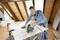 A man is cutting plywood with an electric jigsaw in a workshop. Safety glasses and ear protection are being worn.