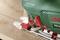 A green Bosch jigsaw cuts precisely across a wooden surface. A built-in lamp illuminates the cutting area.