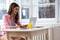 A woman sits smiling at the table, working on her laptop, with a glass of orange juice and a plate of muffins in front of her.