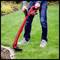 A person is using a red electric lawn trimmer to cut the edge of a green lawn. Plants can be seen in the background.
