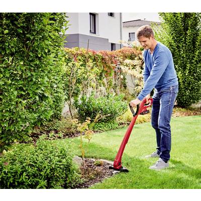 A man in jeans and a blue jumper is using a red lawn trimmer to trim the grass in a well-maintained garden.