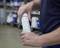 A person is holding an eye wash spray, ready for use. Shelves with various containers are visible in the background.