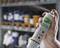 A hand is holding a spray can with the label 'Plum Wound and Eyewash Spray'. Blurred shelves are visible in the background.