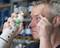 A man sprays eye wash into his eye for cleaning. Liquid drips down his face. Shelves with products are visible in the background.