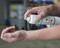 A person is spraying a first aid spray onto their forearm to treat an injury or irritation. A blurred workshop is visible in the background.