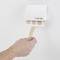 A hand removes a plaster from a white plaster dispenser on the wall. The dispenser shows three visible plasters.