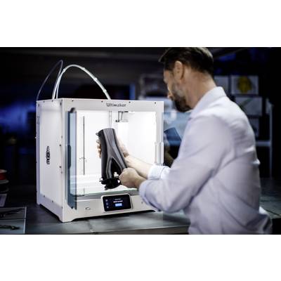 A man removes a black object from a 3D printer in a laboratory. The printer is white and electronically illuminated.
