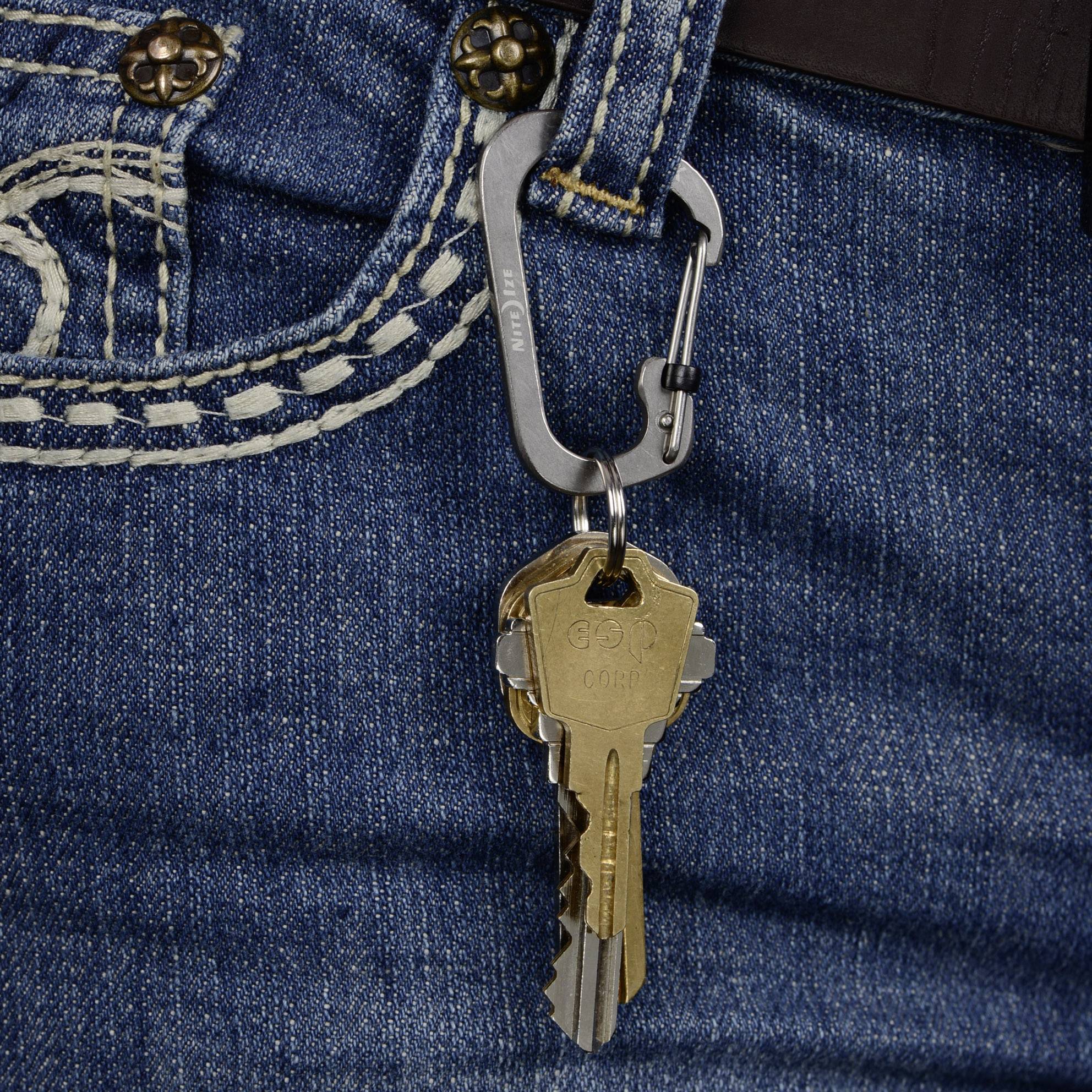 A bunch of keys with two keys hangs from a carabiner clip attached to a jean's belt loop.