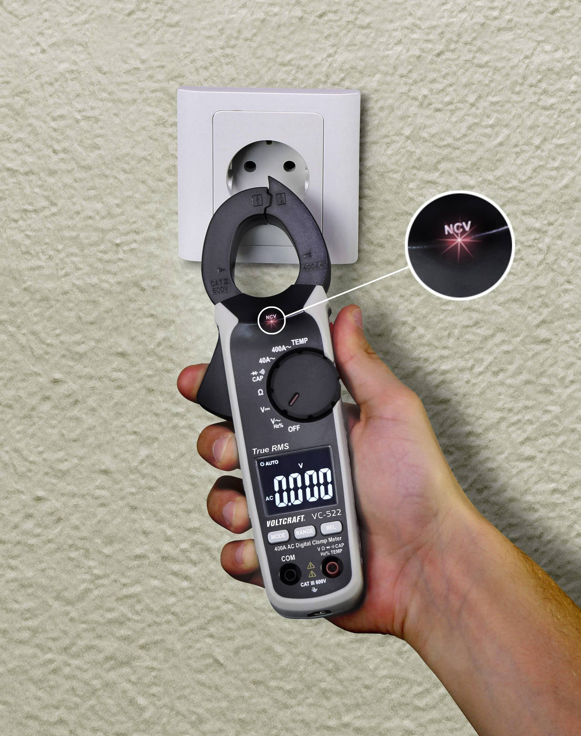 A handheld measuring device is measuring voltage at a power socket. The display shows '0000'. A red light indicates the NCV function.