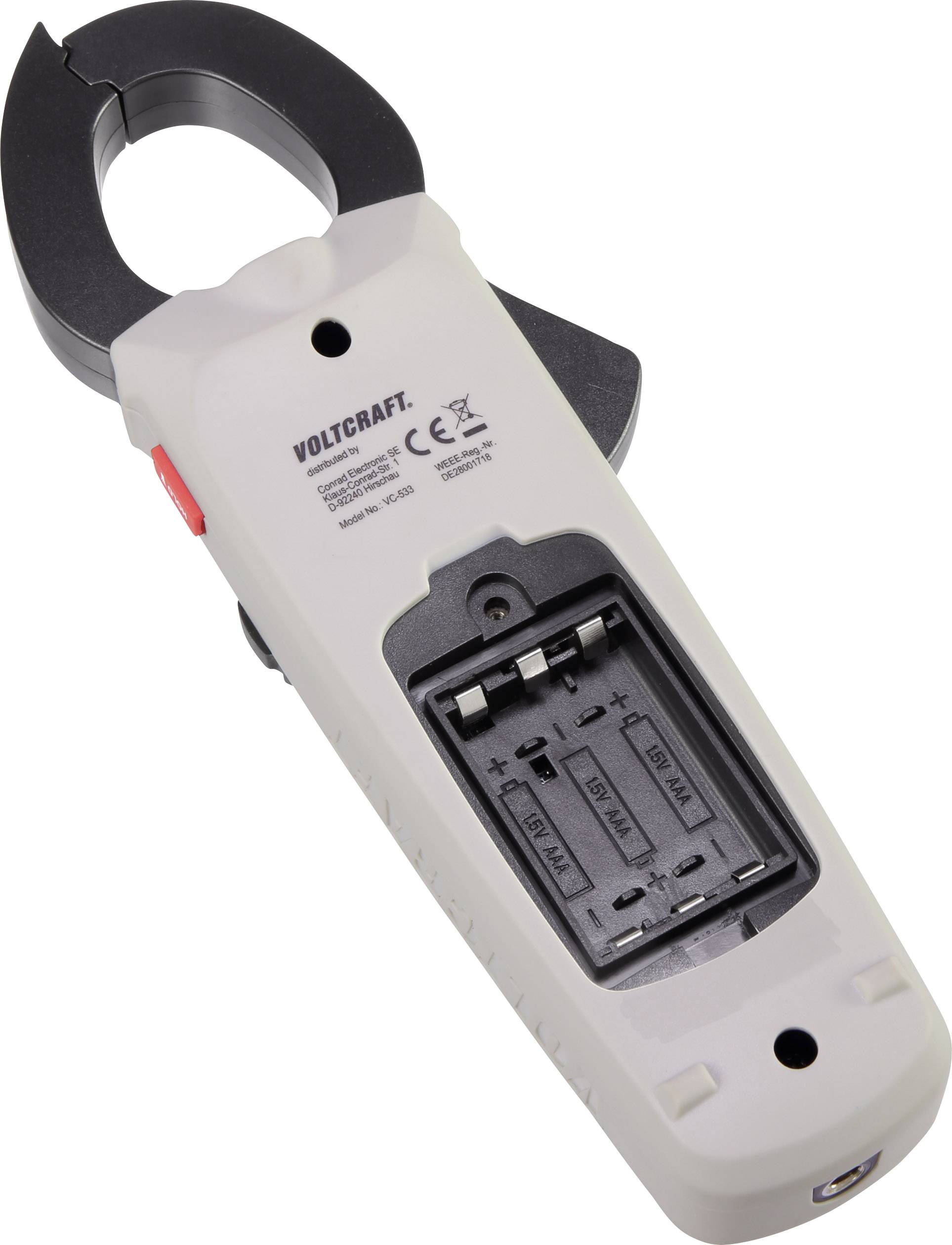 A low-angle view of a beige and black Volcraft current clamp with an open battery cover, revealing space for three AAA batteries.