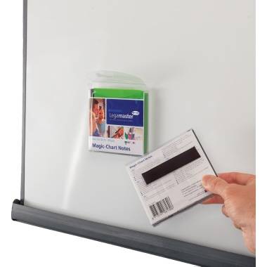 A hand holds a black and white card in front of a packet of Legamaster Magic-Chart sticky notes on a whiteboard.