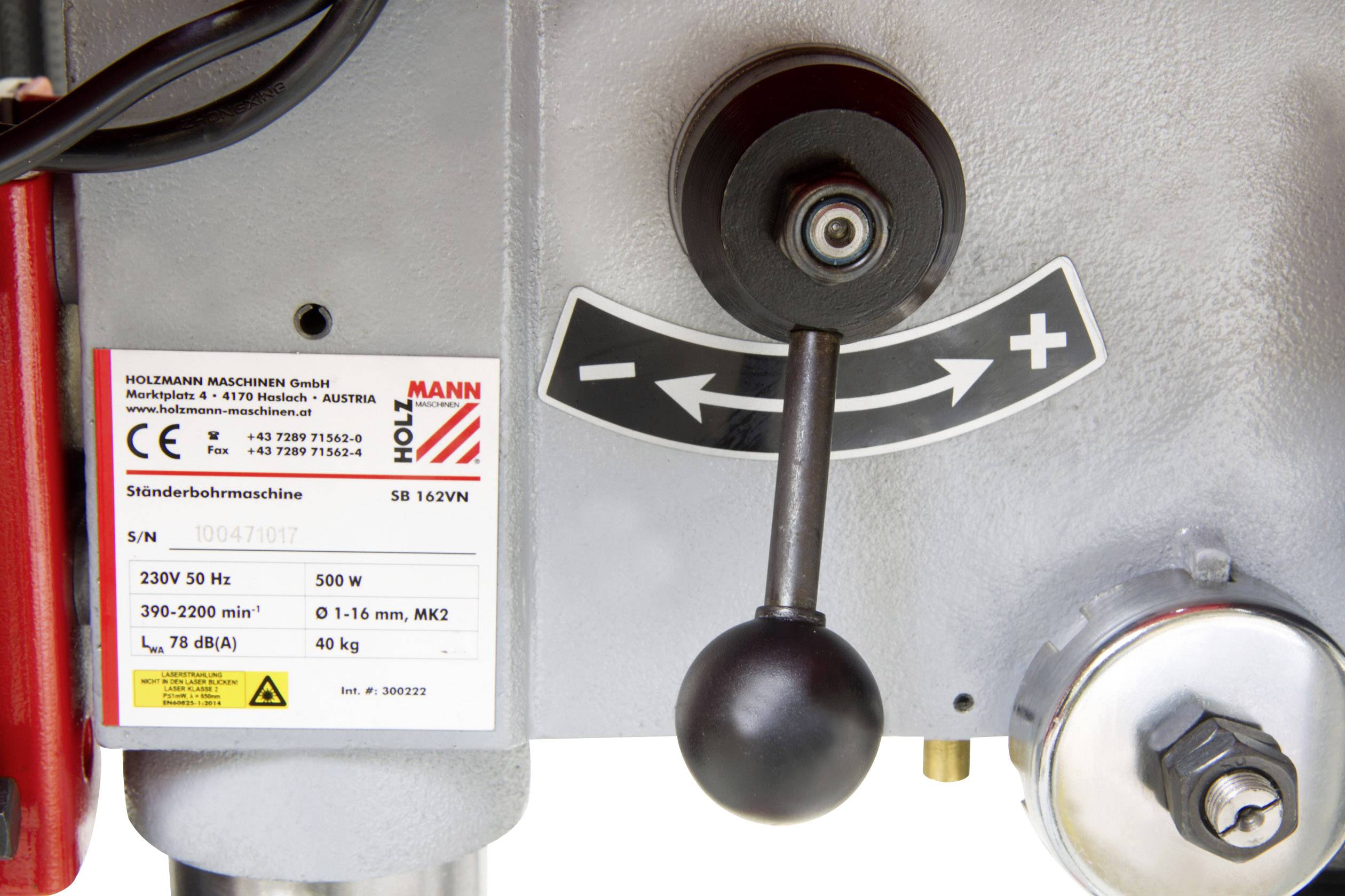 'Control lever and scale with arrows and plus-minus symbols on a pillar drilling machine. Technical information label visible.'