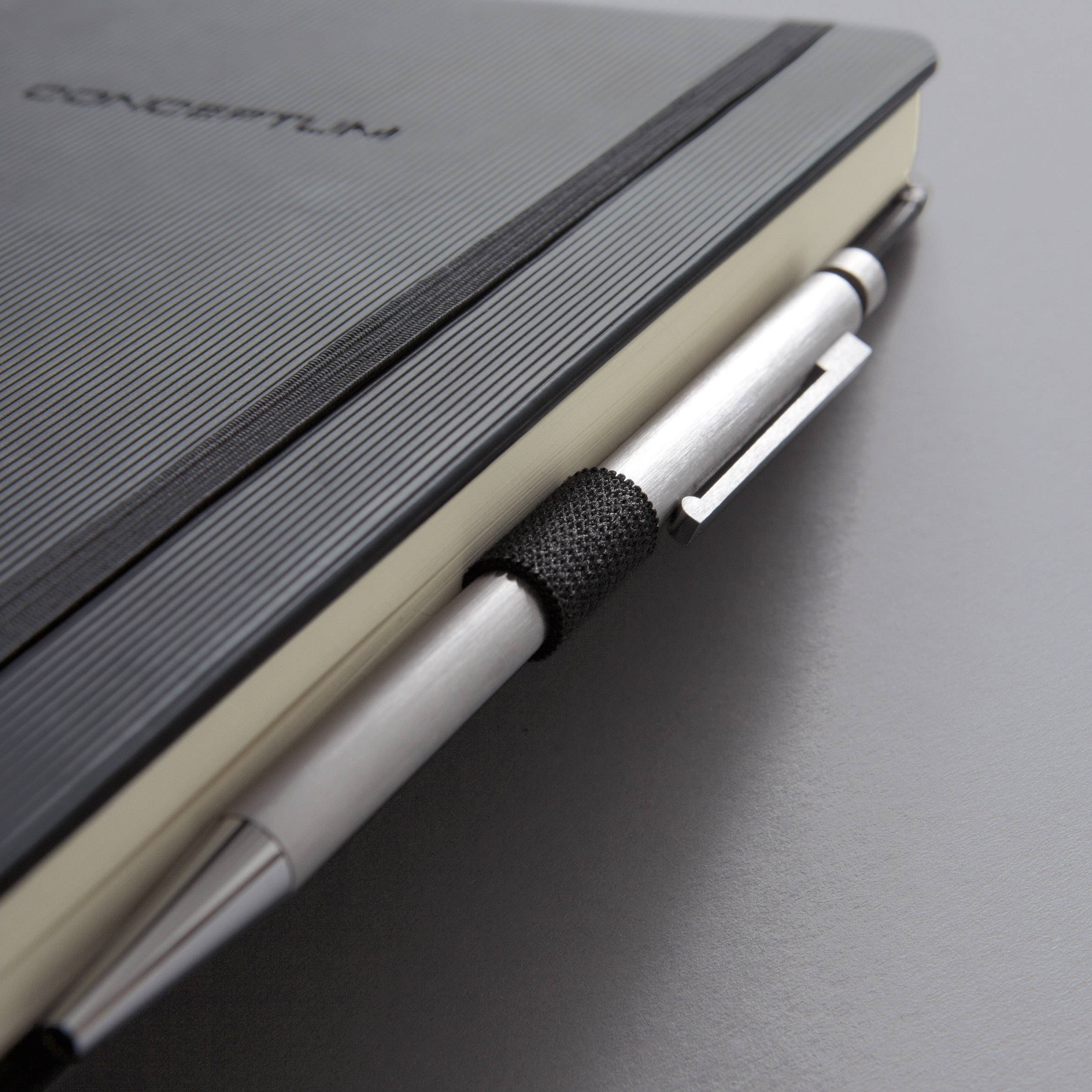 A black notebook with a pen in its holder, lying on a grey table.