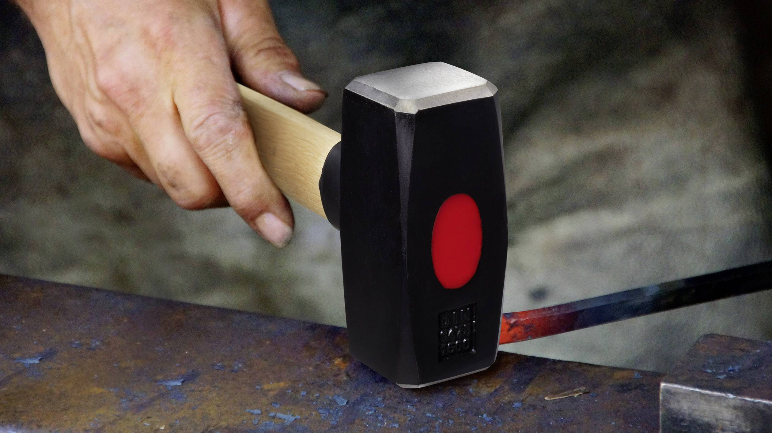 A blacksmith hammers glowing metal with a hammer on an anvil to shape it.