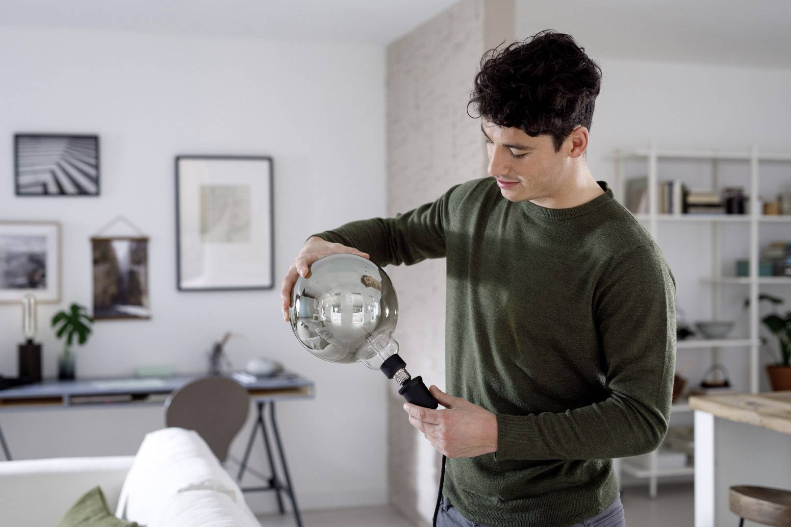 A man is holding a silver sphere in a contemporary living room. Furniture and wall decorations are visible in the background.