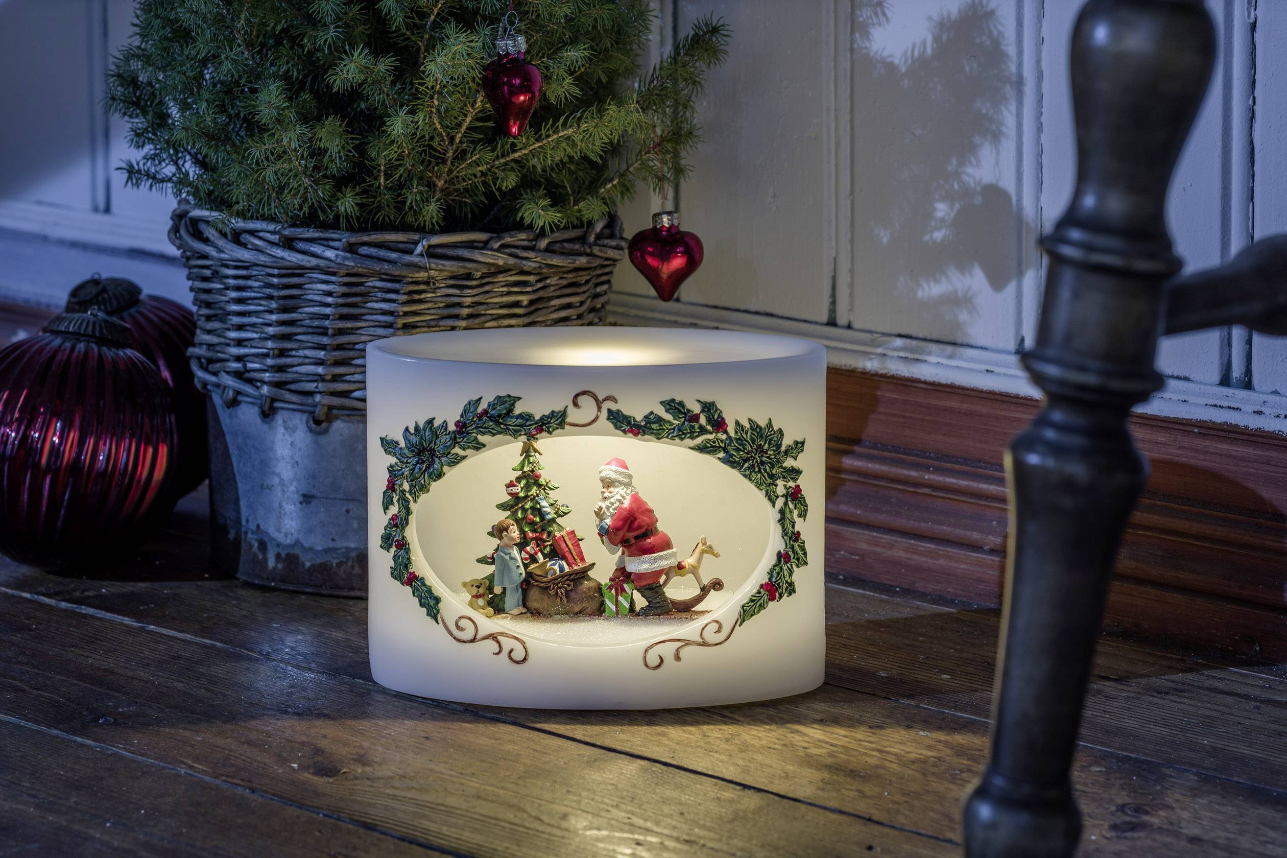 Christmas decorations with an illuminated candle holder, featuring Santa Claus and a tree. Beside it, a Christmas tree in a basket.