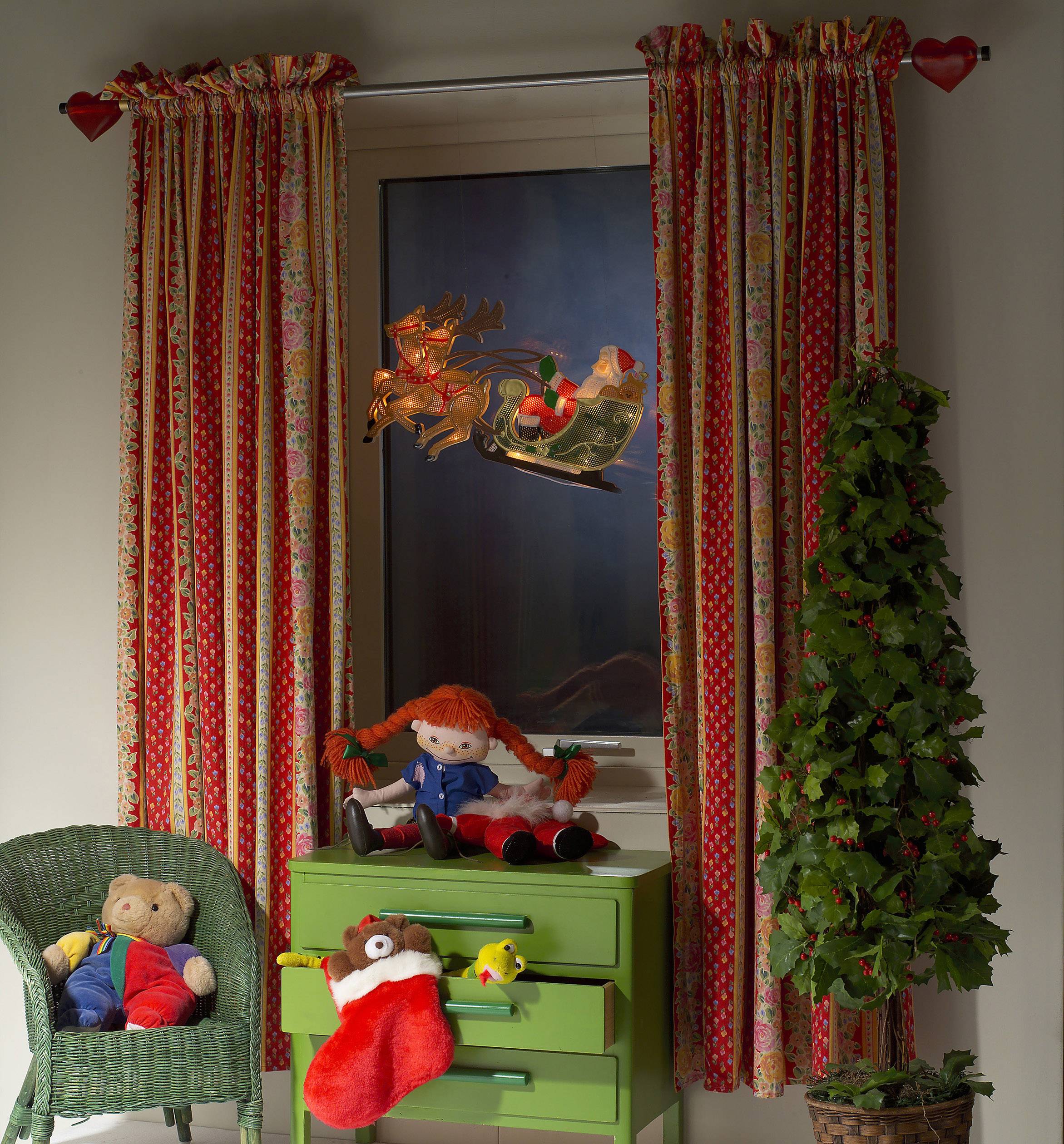 A child's bedroom with a window view, adorned with red curtains. A toy Father Christmas in a sleigh and soft toys around the room.